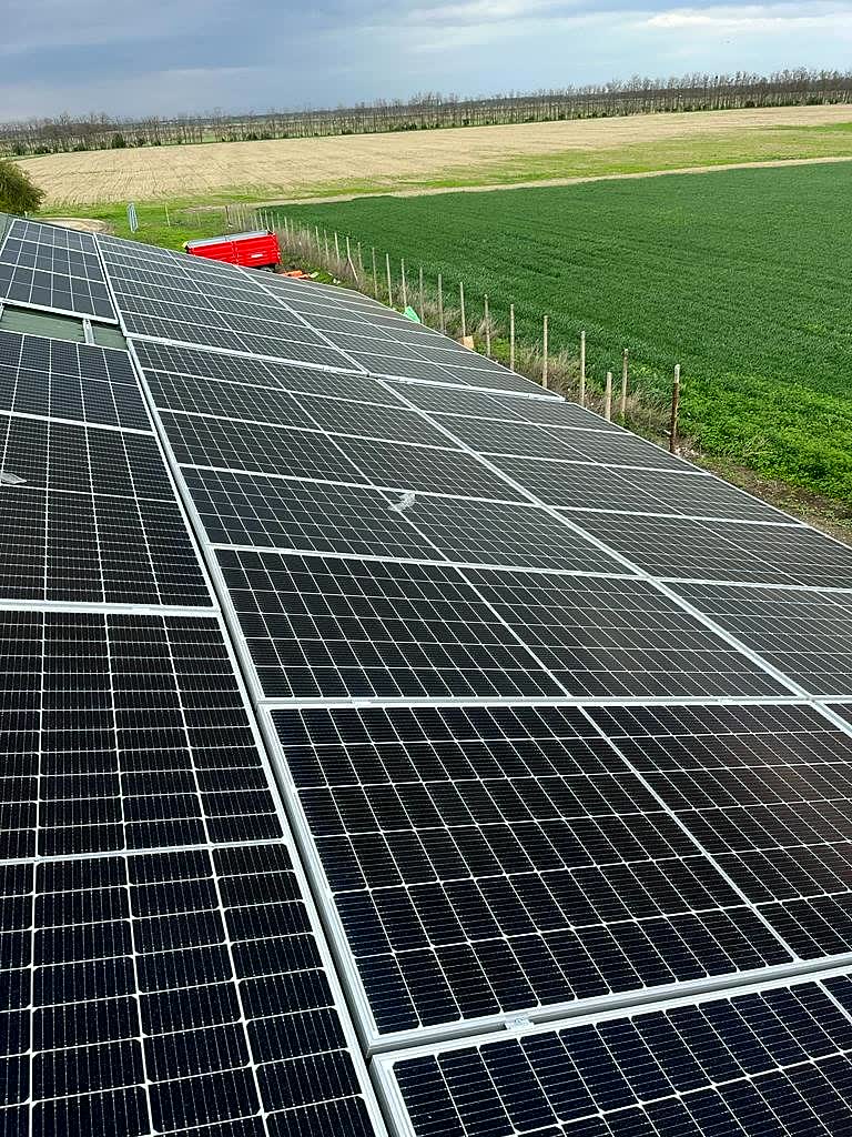 Sistem fotovoltaic hibrid Planservices — panouri pe acoperiș lângă teren agricol